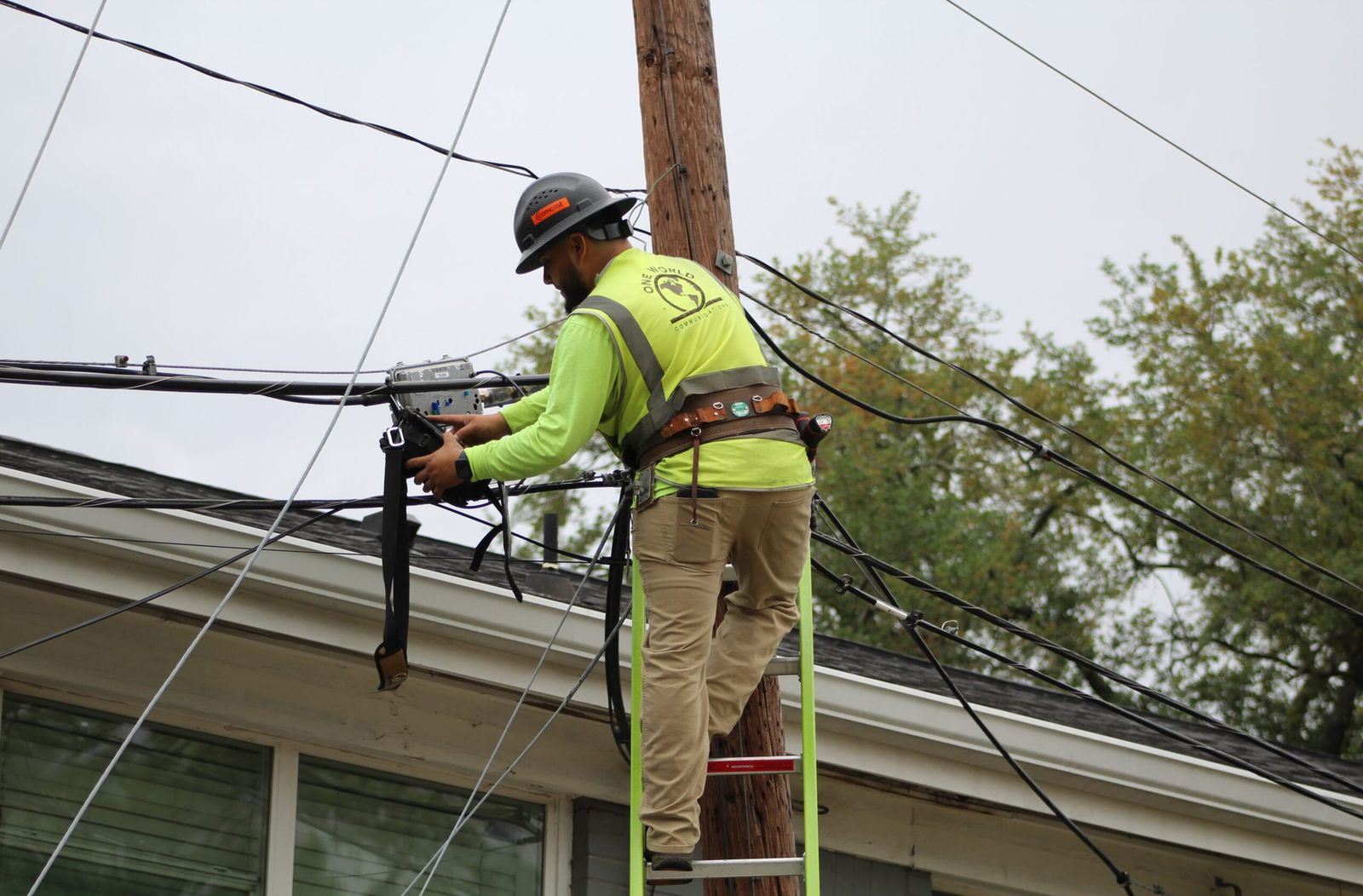 A One World Communications technician working on aerial communications lines on a utility pole