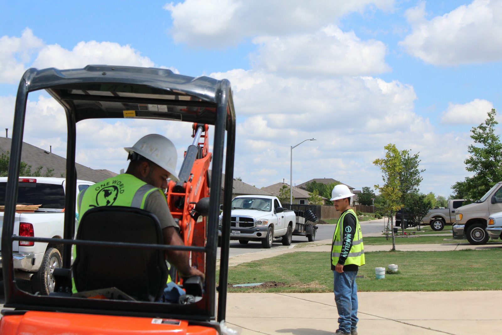 A One World Communications operator running a mini excavator on an underground job with a spotter on the ground